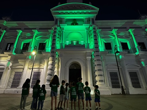 Familias de espaldas frente a un edificio iluminado de verde