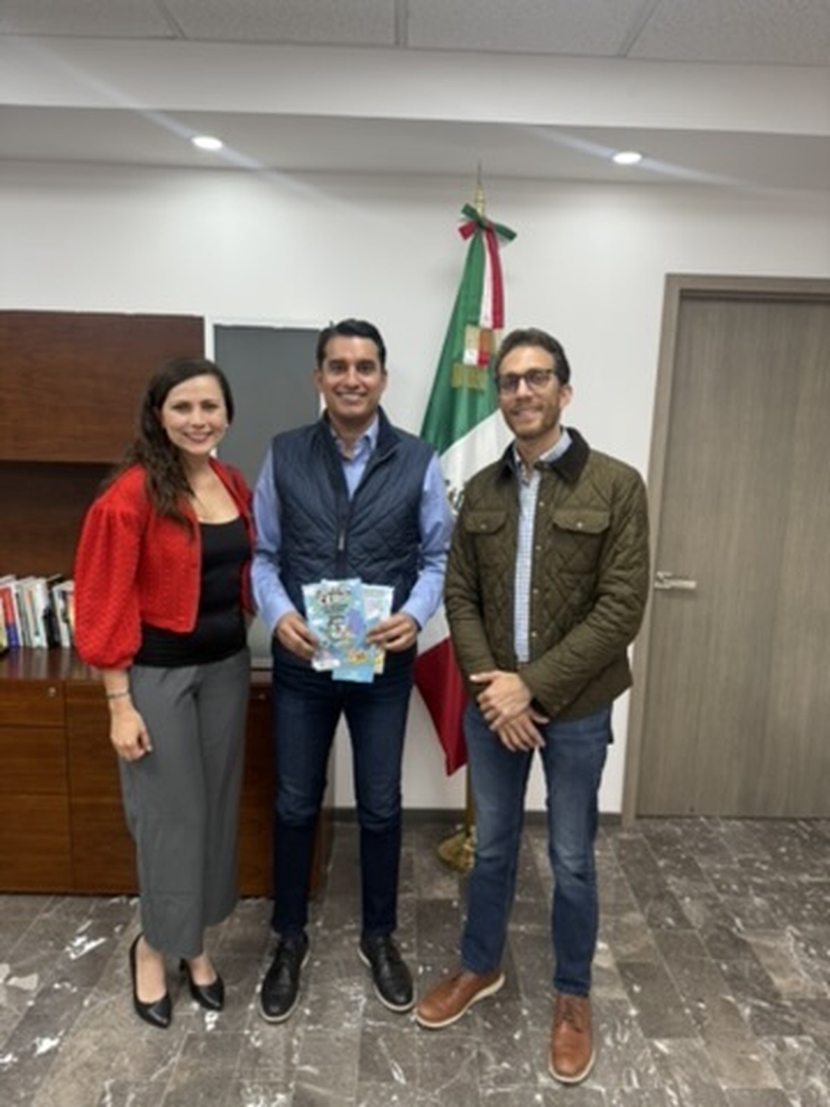 Tres adultos en oficina con bandera de México